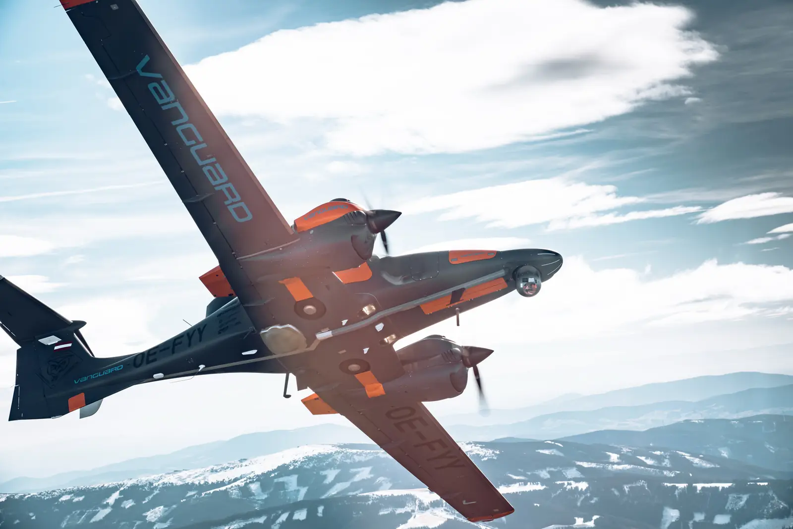 Special mission aircraft with an EO/IR sensor turret under the nose, banking over snow-covered mountains